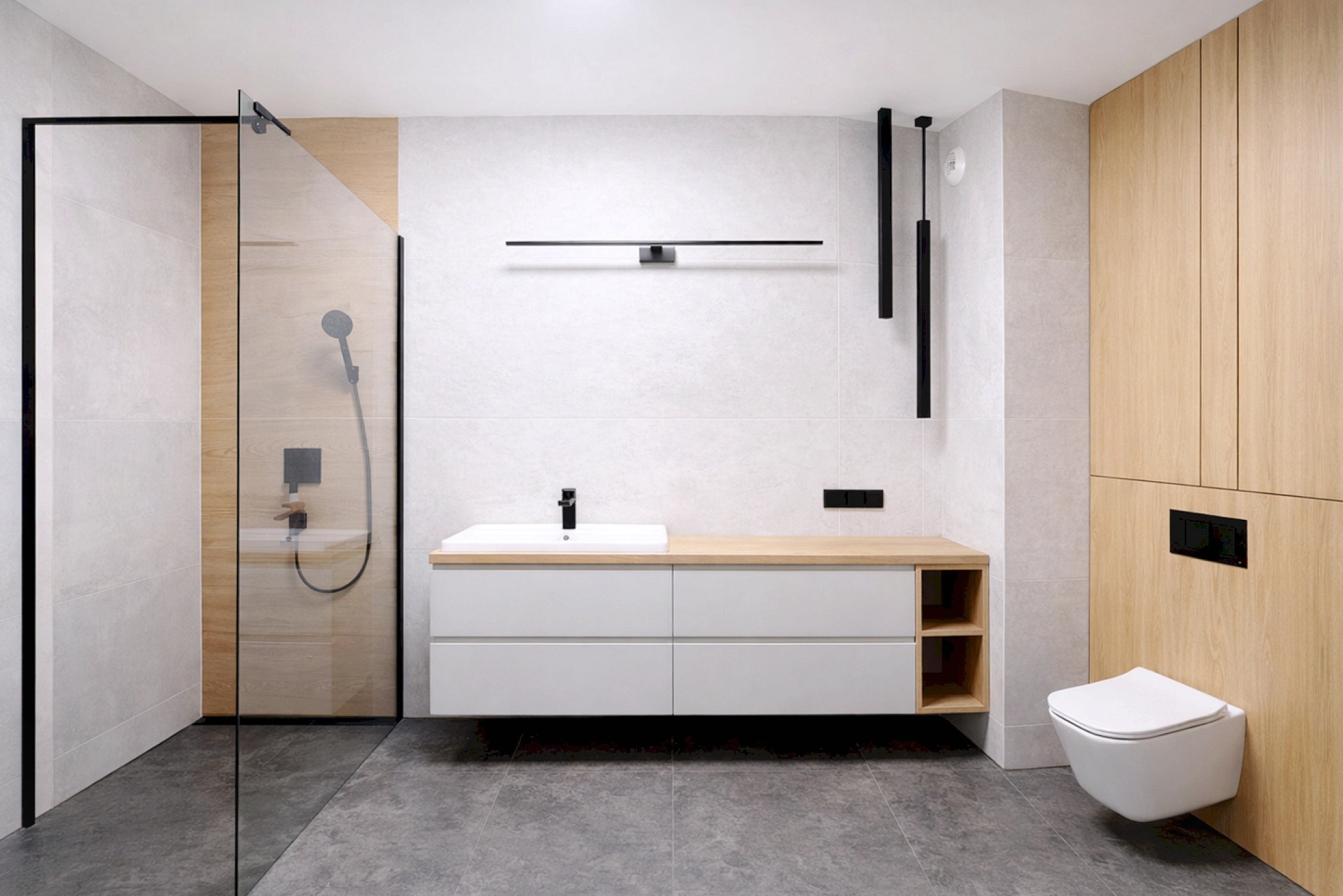 Nowoczesna łazienka z kabiną prysznicową typu walk-in, umywalką nablatową na szafce z drewnianym blatem i podwieszaną toaletą. Minimalistyczne oświetlenie.