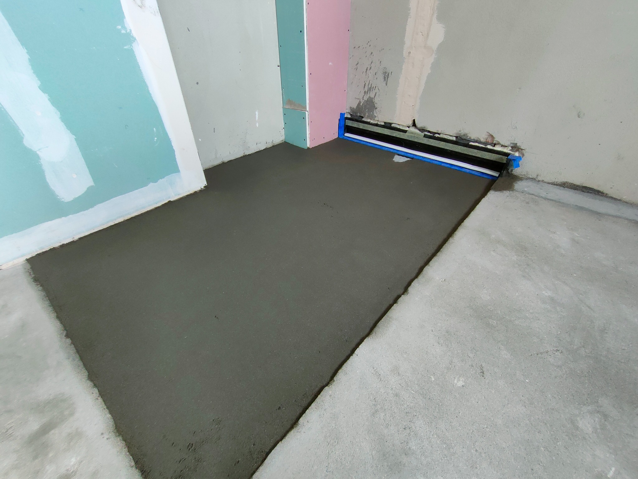 Wylana, świeża wylewka podłogowa w pomieszczeniu z przygotowanymi ścianami do dalszych prac wykończeniowych. Widoczne profile przyścienne.