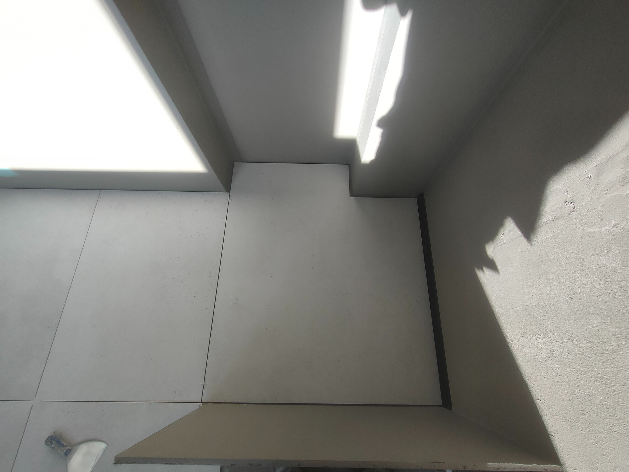 Ukończona podłoga z jasnych, kwadratowych płytek w rogu pomieszczenia. Widoczna szpachelka. Oświetlenie dzienne podkreśla fakturę ściany.