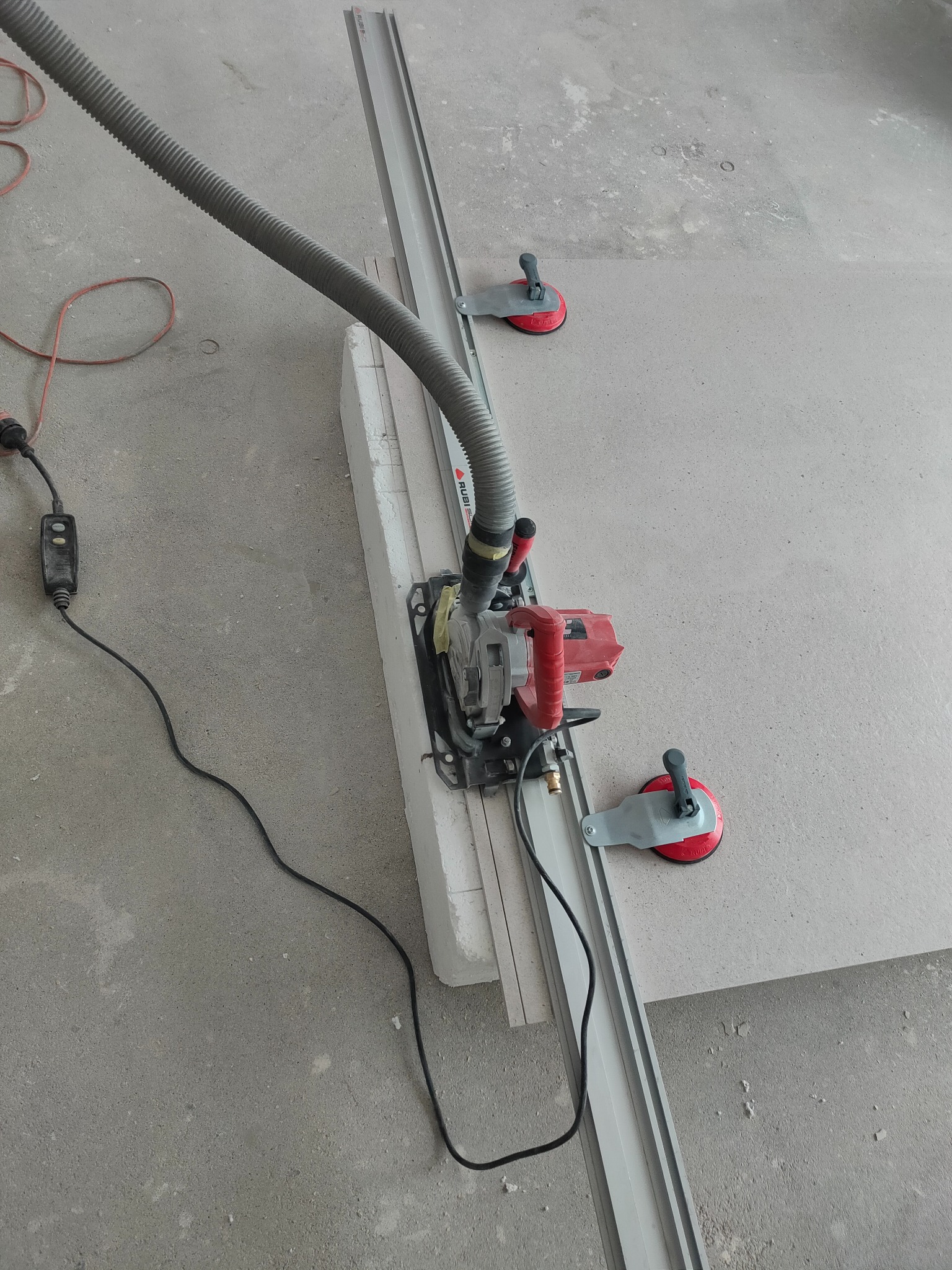 Czerwona piła z odkurzaczem i szyną tnącą Rubi, przymocowana przyssawkami do płyty. Narzędzie do cięcia płytek podczas wykańczania łazienki lub remontu kuchni.