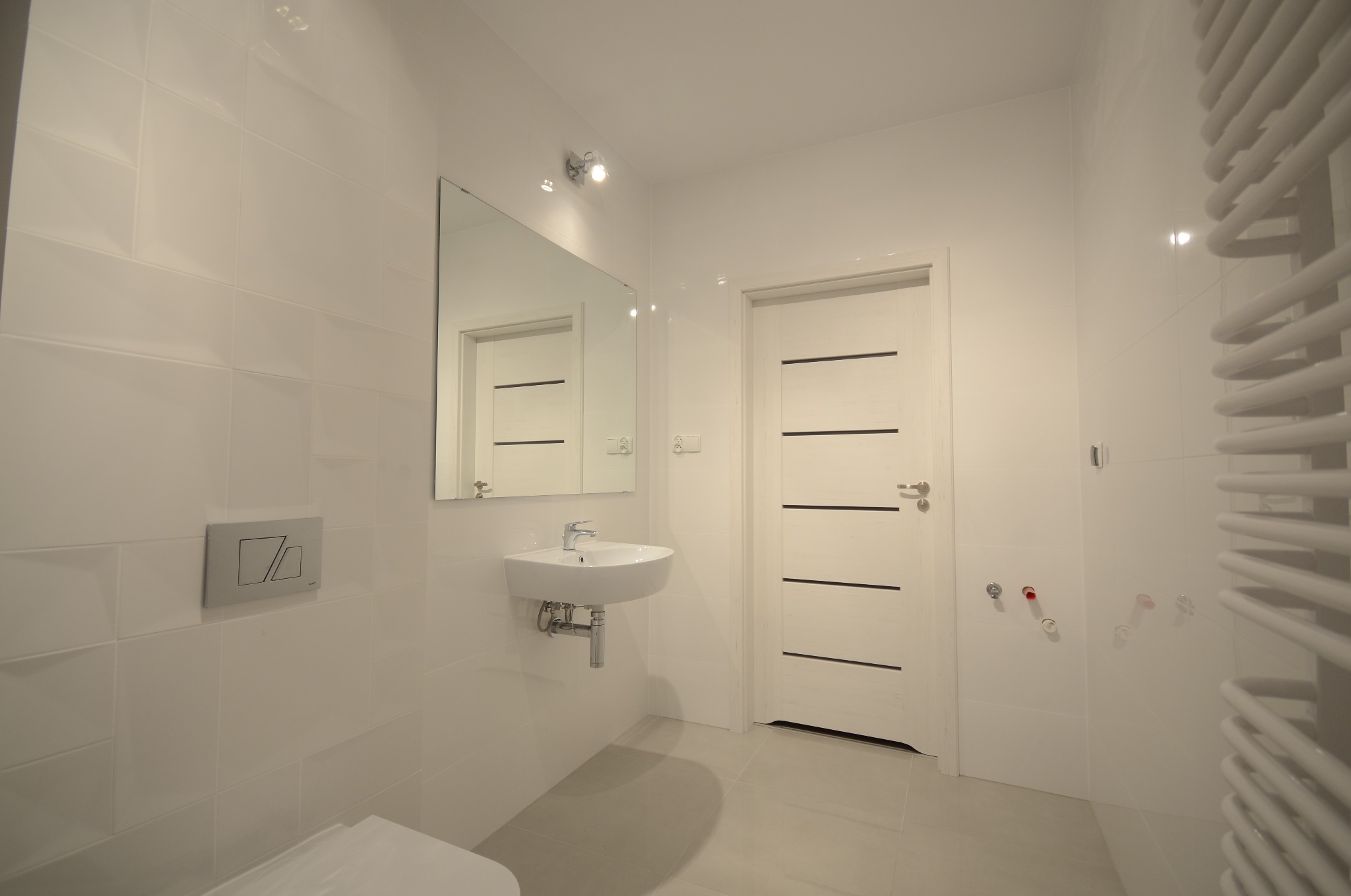 Biała łazienka po remoncie: umywalka, lustro, grzejnik drabinkowy, płytki na ścianach i podłodze. Minimalistyczny design, czystość i nowoczesność.