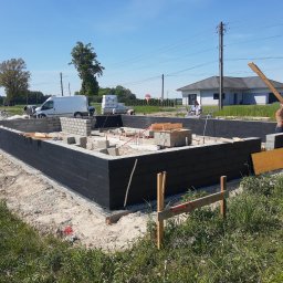 PRAXTON Spółka z o.o. - Wznoszenie fundamentów domu jednorodzinnego: murowane ściany z izolacją, pracownicy w trakcie robót, widoczny sprzęt budowlany i biały van w tle.