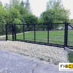 Czarna brama przesuwna z wypełnieniem panelowym FORTE 65, ocynkowana ogniowo i pomalowana na matowy kolor RAL 9005, z widocznym światłem bramy 5 m, prowadząca na trawnik, z podjazdem wysypanym...