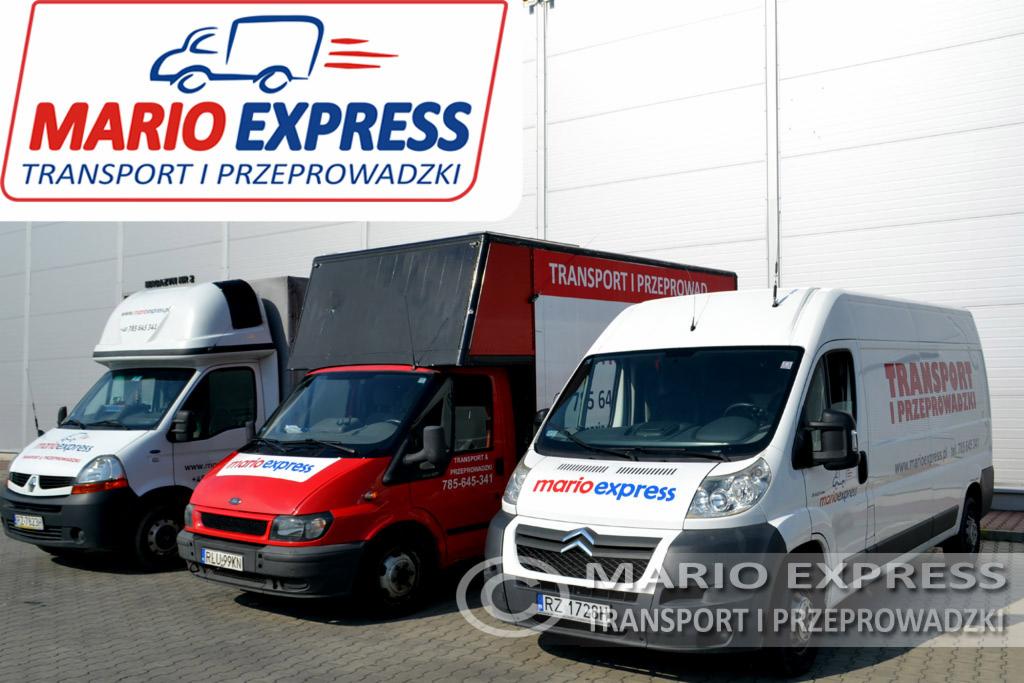 Trzy busy transportowe Mario Express w różnych kolorach (biały, czerwony) zaparkowane przed magazynem. Widoczne logo firmy na każdym z pojazdów.