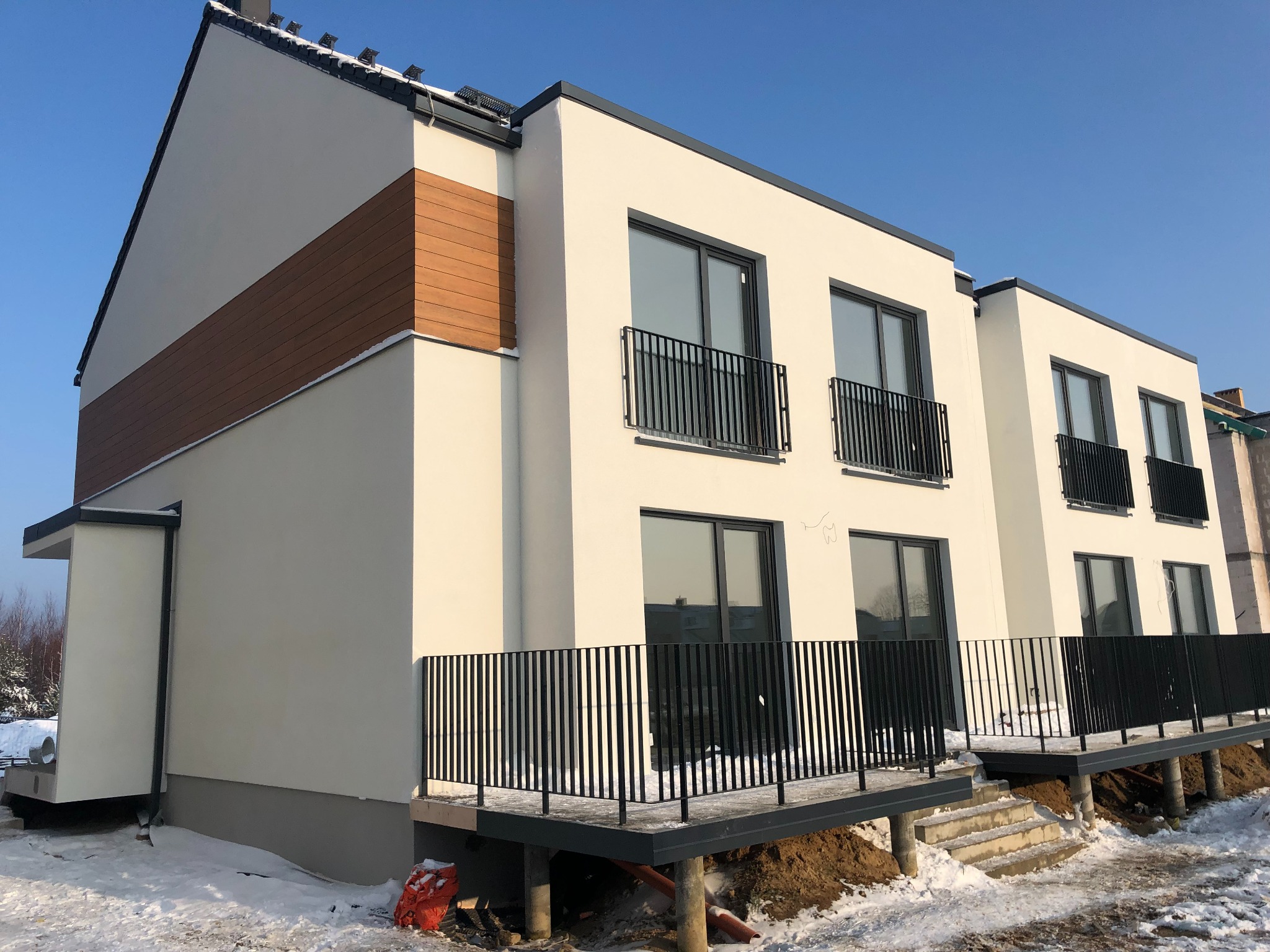 Nowoczesny, dwukondygnacyjny dom z jasną elewacją, drewnianymi akcentami i czarnymi balustradami balkonowymi w zimowej scenerii, ukazujący efekt wykonanych prac.