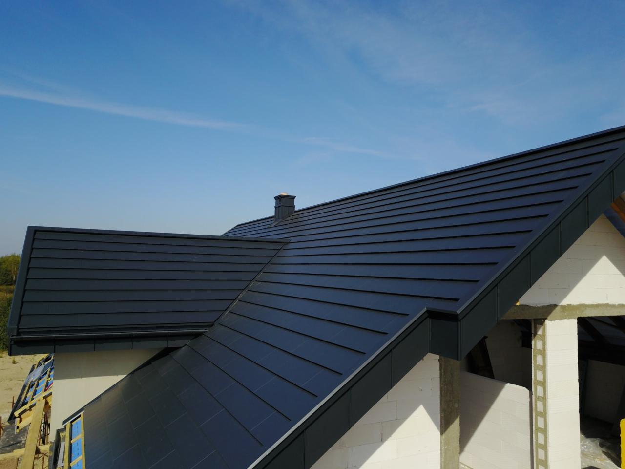 Nowoczesny, grafitowy dach z blachy na domu w trakcie budowy, widok z góry na tle błękitnego nieba.