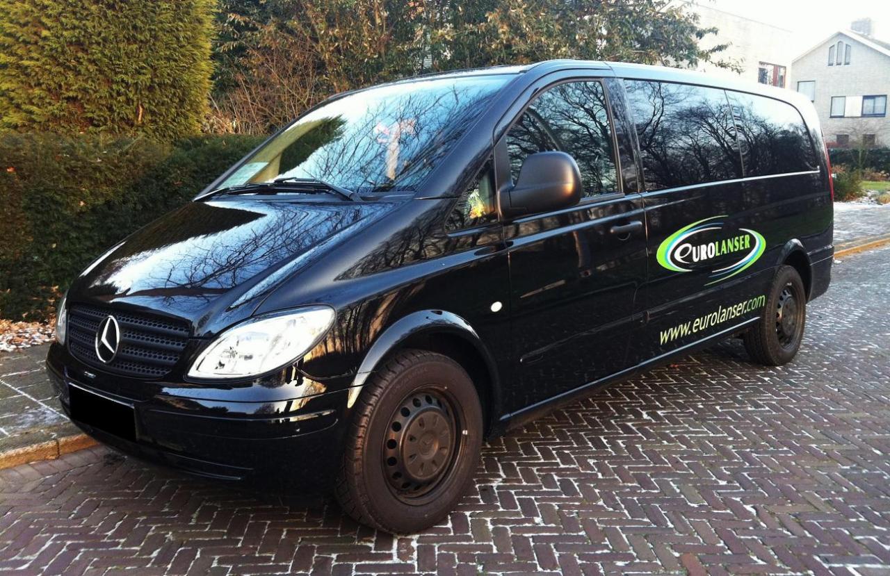 Czarny bus marki Mercedes z logo firmy Eurolanser zaparkowany na brukowanej ulicy, odbicie drzew w szybach.