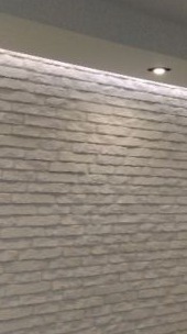 Ściana wykończona dekoracyjną okładziną imitującą kamień w odcieniach szarości i bieli, oświetlona od góry światłem punktowym i listwą LED, tworząca nowoczesny efekt wizualny.