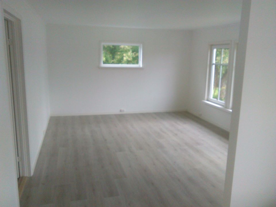 Pusty pokój po remoncie z położonymi panelami podłogowymi w odcieniach szarości, widoczne dwa okna z białymi ramami i białe ściany.