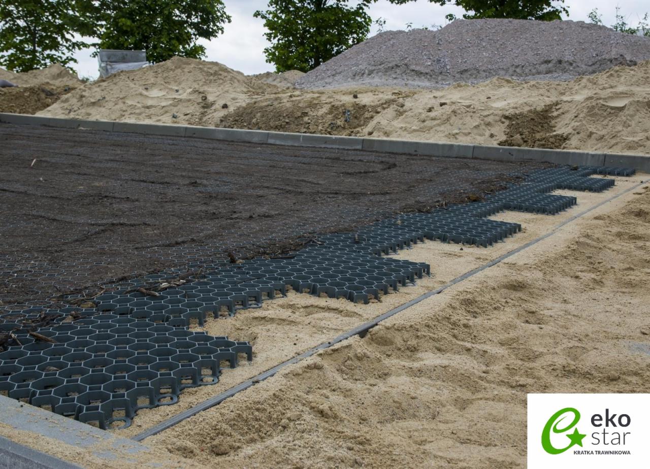 Przygotowanie podłoża pod nawierzchnię z kratki trawnikowej Eko Star w Elblągu, widoczna warstwa piasku, geowłókniny i częściowo ułożona kratka, w tle hałda piasku i kamienia.