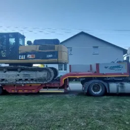 Ciężarówka z naczepą niskopodwoziową przewożąca dużą koparkę gąsienicową CAT 336D, widoczna tablica z nazwą firmy przewozowej.