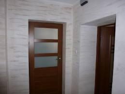 Poddasze po adaptacji: ściany wykończone dekoracyjnym tynkiem imitującym drewno, drewniane drzwi z przeszkleniami oraz fragment drugich drzwi w ościeżnicy.