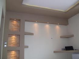 Ściana z wnękami oświetlonymi ciepłym światłem, półki z dekoracjami, sufit podwieszany z oświetleniem punktowym.