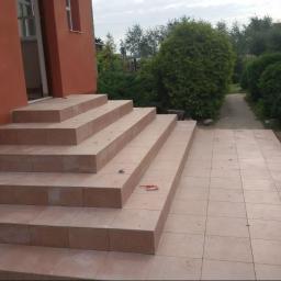 Landmen Firma ogólnobudowlana - Wykończone kafelkami schody wejściowe do domu z pomarańczową elewacją, widoczny fragment terakoty przed schodami i ścieżka w ogrodzie w tle, na jednym ze stopni leży śrubokręt.