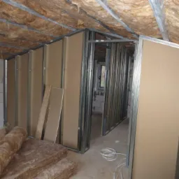 Montaż ścian działowych z płyt kartonowo-gipsowych na metalowym stelażu w surowym wnętrzu poddasza z ociepleniem wełną mineralną.