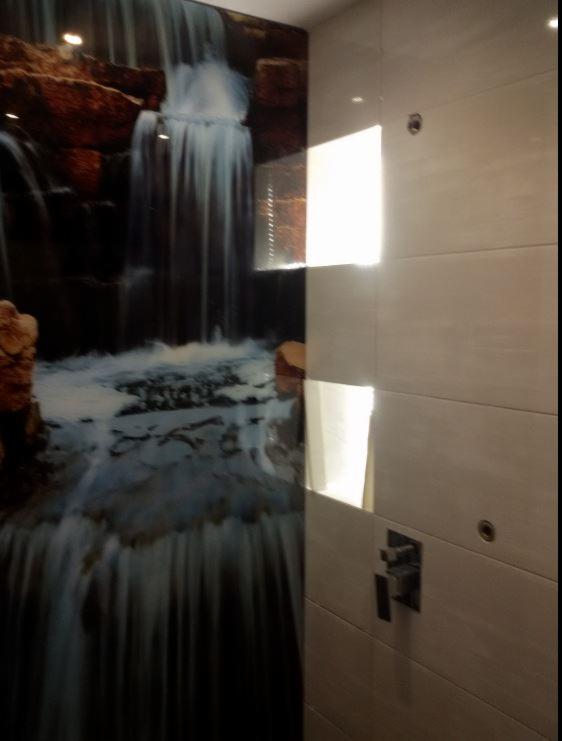 Wykończona ściana w łazience z jasnymi, poziomymi płytkami i armaturą; na sąsiedniej ścianie fototapeta z motywem wodospadu.