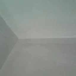 Gładka, jasnoszara ściana i sufit po nałożeniu tynku maszynowego, widoczny narożnik pomieszczenia, oświetlenie z góry tworzy delikatne cienie.