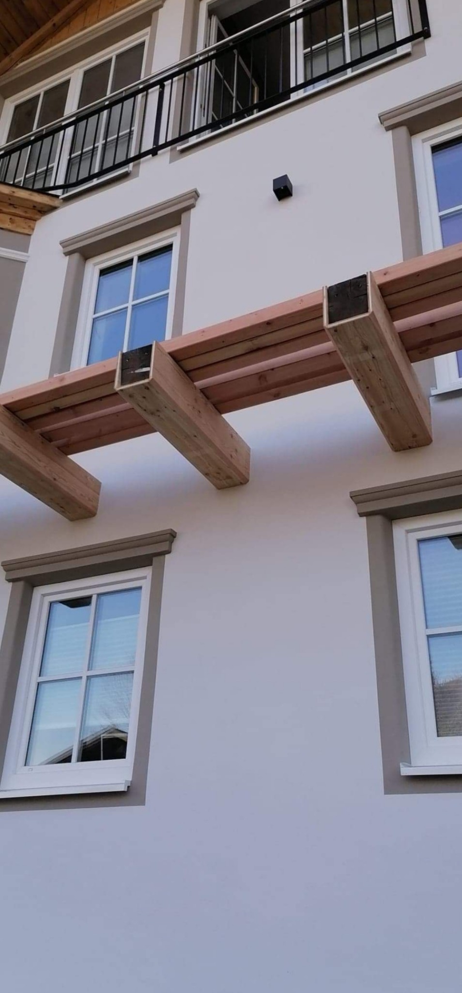 Elewacja budynku z oknami w białych ramach i drewnianą konstrukcją dekoracyjną nad nimi, widok z dołu.