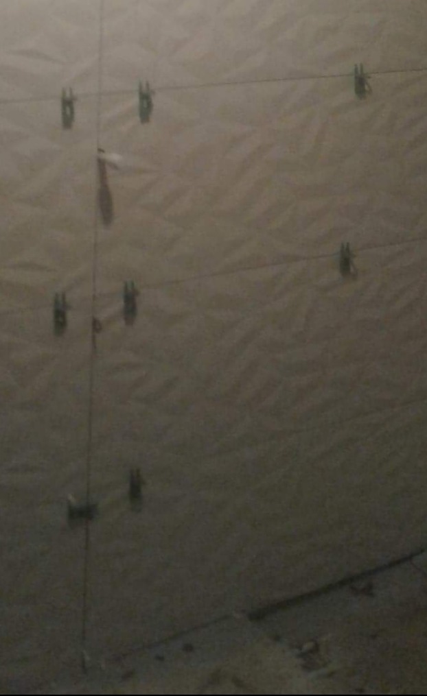 Ściana z przyklejonymi płytkami, poziomowana za pomocą sznurka i klipsów, widoczne nierówności na powierzchni płytek.