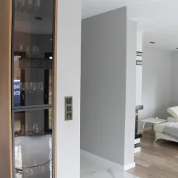 Nowoczesne wnętrze: szara ściana, biały narożnik z kocem w gwiazdy, przeszklona witryna z oświetleniem i włączniki światła w ramce.