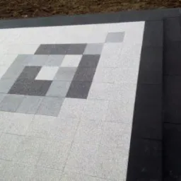 Ułożona kostka brukowa w jasnych odcieniach szarości z geometrycznym wzorem w ciemniejszych szarościach, obramowana czarną kostką.