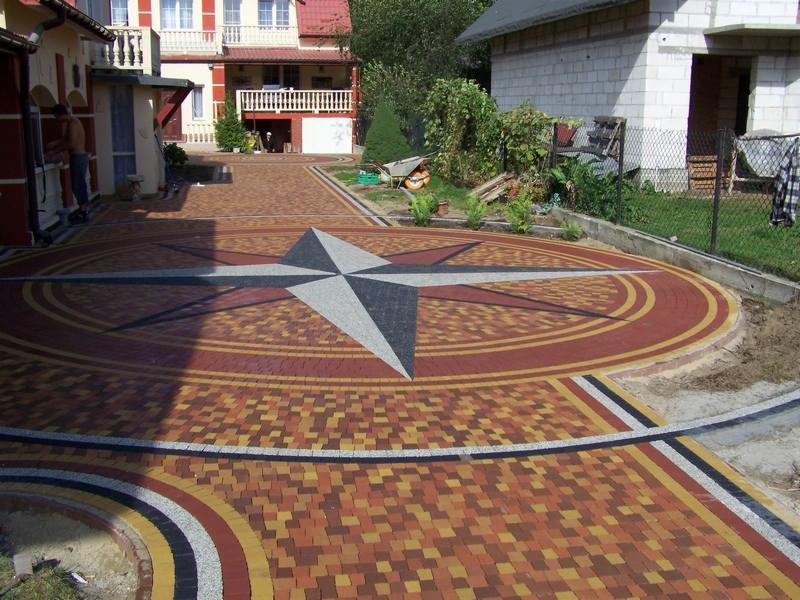 Kolorowa nawierzchnia z kostki brukowej ułożona w wzór kompasu na podjeździe przed domem.