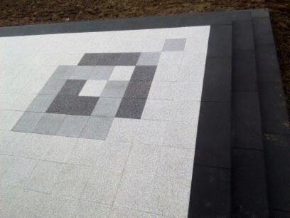 Ułożona kostka brukowa w jasnych odcieniach szarości z geometrycznym wzorem w ciemniejszych szarościach, obramowana czarną kostką.