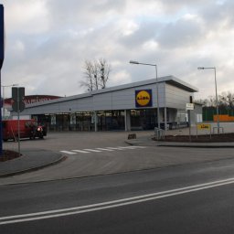 BEAR Polska - Widok zewnętrzny sklepu Lidl z parkingu i ulicy w pochmurny dzień. Na parkingu zaparkowane samochody i furgonetka.