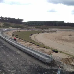 Budowa drogi: Widok na plac budowy z ułożonym krawężnikiem, przygotowanym terenem pod nawierzchnię i nasadzoną trawą na zboczu.