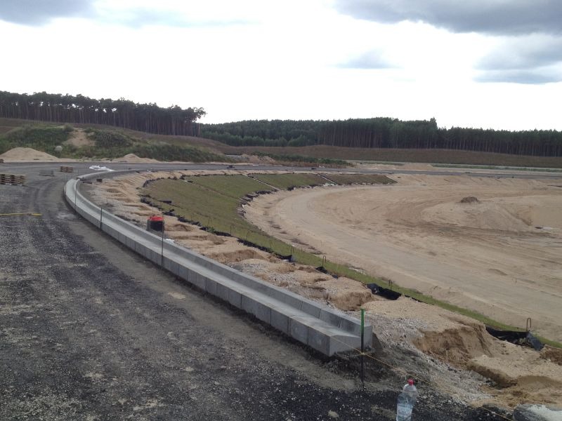 Budowa drogi: Widok na plac budowy z ułożonym krawężnikiem, przygotowanym terenem pod nawierzchnię i nasadzoną trawą na zboczu.