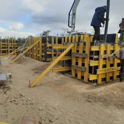 BUDMAR Rosiński Marek - Budowa fundamentów w Pogorzeli: Żółte szalunki zbrojeniowe, robotnicy przy pracy, na drugim planie betonowóz z pompą do betonu.