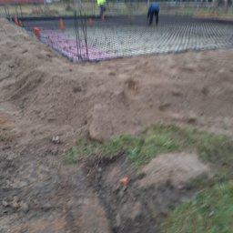 BUDMAR Rosiński Marek - Przygotowanie terenu pod budowę domu: widoczne fundamenty z szalunkiem, zbrojenie pionowe, warstwa izolacyjna z różowego styropianu, pracownicy w tle.