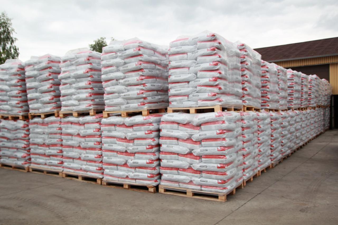 Rzędy palet z workami, prawdopodobnie z opałem, ustawione równo w magazynie. Worki owinięte folią, widoczny fragment budynku w tle.