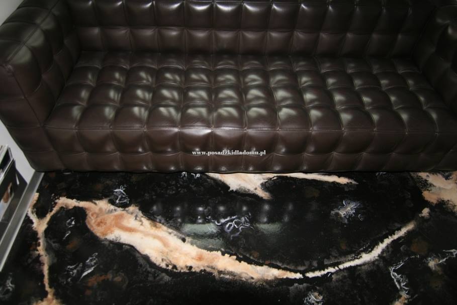 Ciemnobrązowa, pikowana sofa na czarnej posadzce z wzorem imitującym marmur. Widoczny fragment sofy i podłogi, podkreślający unikalny design wnętrza.