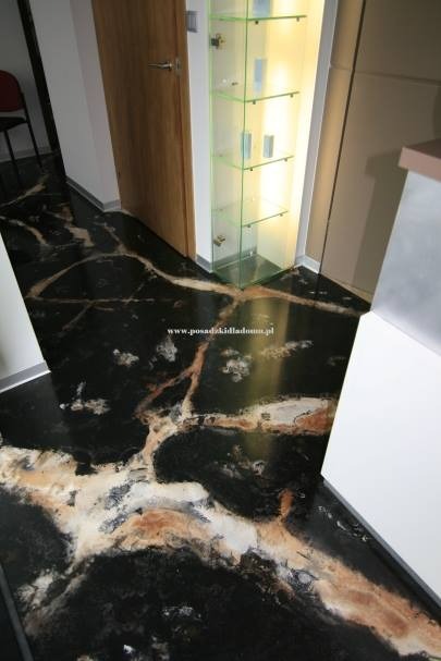 Błyszcząca, czarna posadzka z marmurkowym wzorem w odcieniach bieli i brązu, widoczna przy drzwiach i szklanej witrynie. Nietypowy wzór i połysk dodają elegancji.