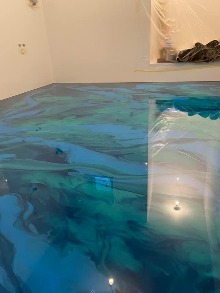 Błyszcząca, turkusowo-niebieska posadzka żywiczna z efektem marmuru w jasnym pomieszczeniu, zabezpieczone ściany folią malarską. Nowoczesne wykończenie podłogi.