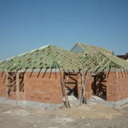 Budowa domu jednorodzinnego w trakcie montażu konstrukcji więźby dachowej z drewna, widoczne pustaki ceramiczne ścian i drabina oparta o budynek.