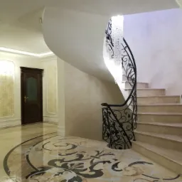 Eleganckie wnętrze z krętymi schodami, ozdobną balustradą i kryształowym żyrandolem w holu w Krakowie. Podłoga z marmurowym wzorem.