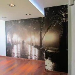 Fototapeta przedstawiająca nocny park z oświetlonymi latarniami i spacerującą parą, zamontowana na ścianie w pomieszczeniu z parkietem i nowoczesnym oświetleniem sufitowym.