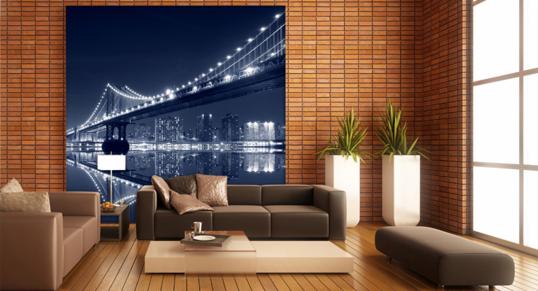 Salon z ceglaną ścianą, na której wisi fototapeta przedstawiająca nocny widok na oświetlony most i panoramę miasta odbijającą się w wodzie. Wnętrze uzupełniają sofy w odcieniach brązu, białe...