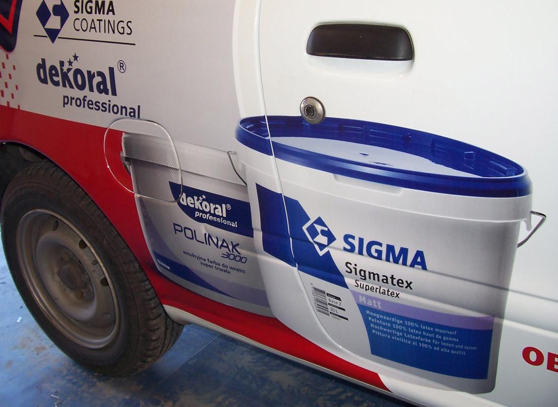 Biały samochód z reklamowym nadrukiem farb Dekoral i Sigma na karoserii, widoczne detale nadruku i fragment opony.