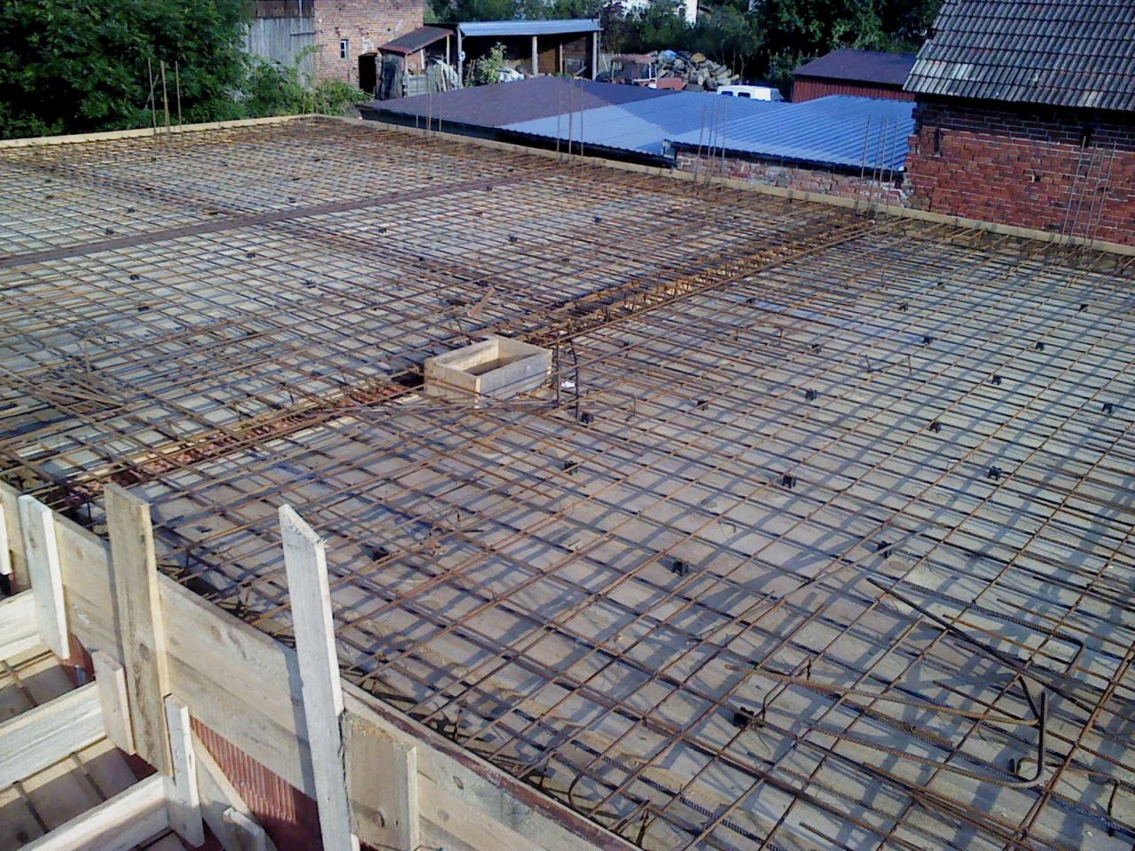 Zbrojenie płyty fundamentowej z drewnianym szalunkiem, widok z góry. Stalowa siatka zbrojeniowa na betonowej powierzchni, przygotowana do zalania betonem. Budowa domu.