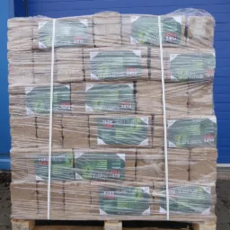 Paleta z brykietem drzewnym Pure Fire, owinięta folią, z etykietami w języku polskim, na tle niebieskiej ściany. Widoczne elementy roślinności.