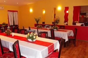 Sala bankietowa z długimi stołami udekorowanymi białymi obrusami, czerwonymi bieżnikami i bukietami białych róż. Krzesła w kolorze ciemnej wiśni z czerwonymi poduszkami. Żółte ściany i drewniana...