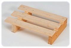 Niewielka, jasna paleta z surowego drewna, trzy deski na dwóch poprzeczkach i podstawie, widoczna faktura drewna i gwoździe, neutralne tło.