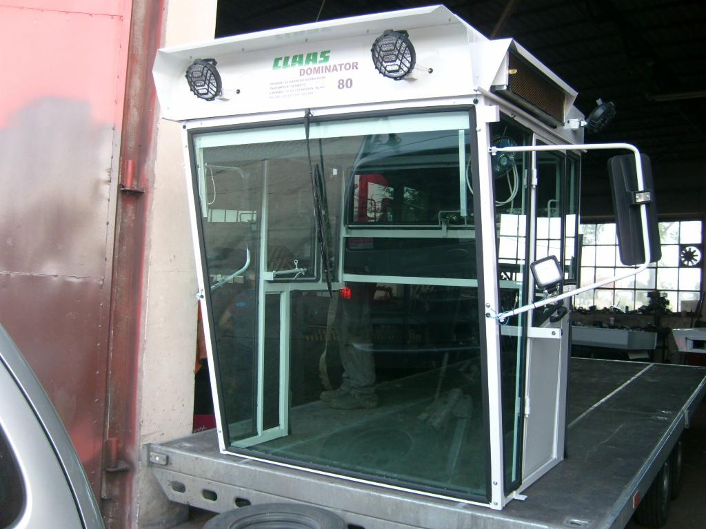 Kabina kombajnu Claas Dominator 80 z widocznymi szybami, reflektorami i lusterkiem, umieszczona na platformie transportowej.
