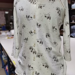 Ciach ciach - Jasna bluzka z długim rękawem, zapinana na guziki, w dziecięcy wzór z buldogami francuskimi i gwiazdkami, prezentowana na manekinie w szwalni.