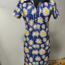 Sukienka w kwiaty na manekinie, krótki rękaw, styl retro z lat 70., niebieska tkanina w białe i żółte stokrotki. Widoczne detale wykończenia i krój.