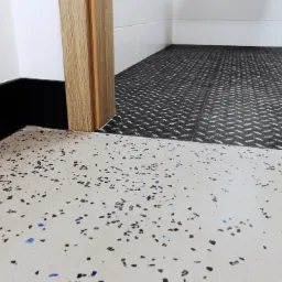 Fragment podłogi z żywicy epoksydowej w neutralnym odcieniu z kolorowymi wtrąceniami, przechodzącej w podłogę z blachy ryflowanej w nowym pomieszczeniu.