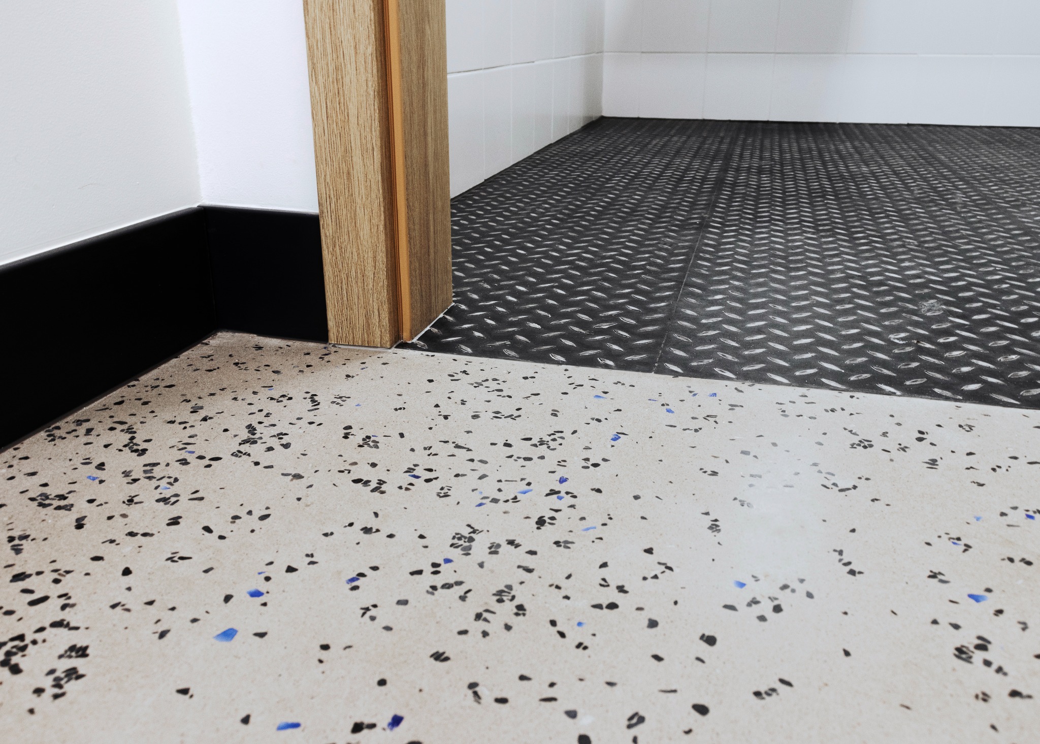 Fragment podłogi z żywicy epoksydowej w neutralnym odcieniu z kolorowymi wtrąceniami, przechodzącej w podłogę z blachy ryflowanej w nowym pomieszczeniu.